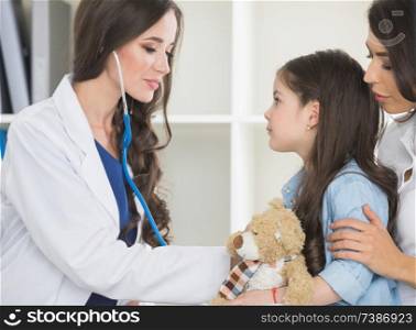 Pediatrician checks heart beat of a little girl in the arms of mother. Pediatrician and little girl in