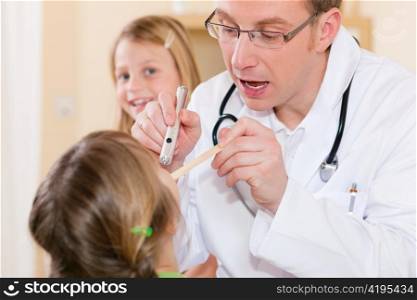 Pediatrician doctor examining throat of a girl, in the background her sister is waiting to be examined as well