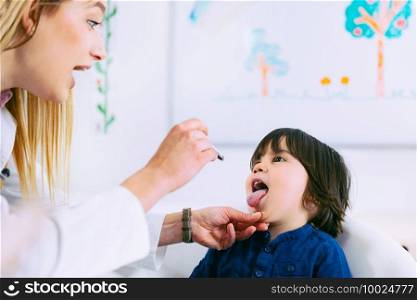Pediatrician examining little boy’s throat with pen torch