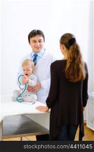 Pediatrician talking with mother while baby playing with stethoscope &#xA;