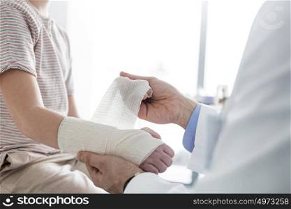Pediatrician tying bandage on boy hand at clinic