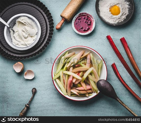 Peeled and sliced rhubarb in bowl on kitchen table background with with cooking and baking tools, top view. Seasonal food concept. Rhubarb cake preparation.