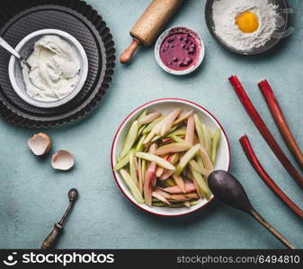 Peeled and sliced rhubarb in bowl on kitchen table background with with cooking and baking tools, top view. Seasonal food concept. Rhubarb cake preparation.