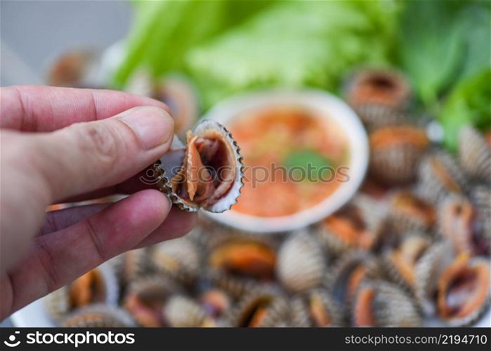 Peeled cockles on hand with seafood sauce and vegetable salad lettuce on plate background, Fresh raw shellfish blood cockle ocean gourmet seafood in the restaurant, sea shells food