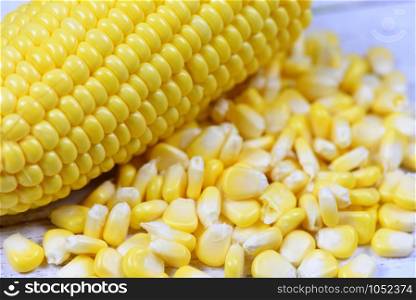 Peeled ear of corn on the cob and corn seeds on white wooden background