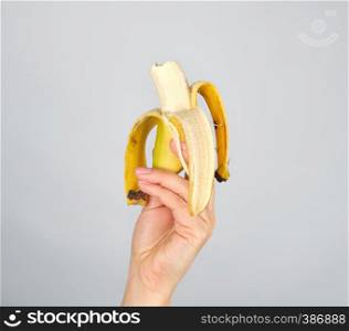 peeled fresh banana in a female hand on a white background, fruit is bitten off