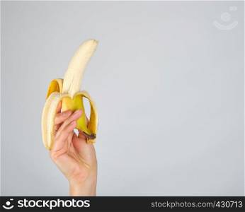 peeled fresh yellow banana in female hand on white background, copy space