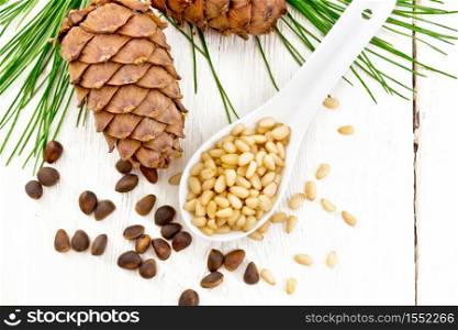Peeled kernels of cedar nuts in a spoon, two pinecones and nuts in the shell against a light wooden board on top