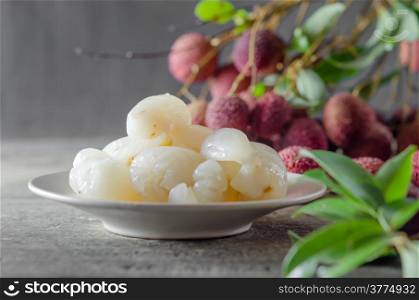 peeled lychee fruit on dish with leaves on a wooden table. Lychee fruit