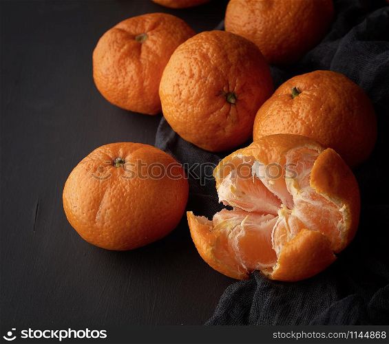 peeled ripe orange mandarin and a bunch of unpeeled round whole fruits on a black napkin, low key