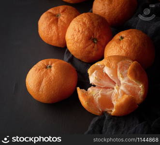 peeled ripe orange mandarin and a bunch of unpeeled round whole fruits on a black napkin, low key