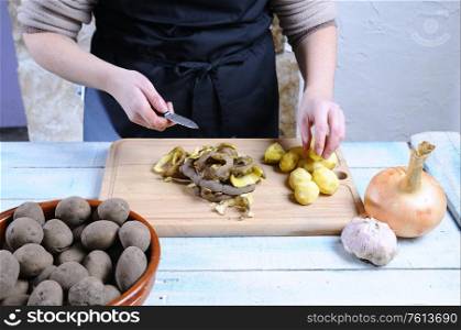 Peeling potatoes on wooden table in the kitchen.&#xA;