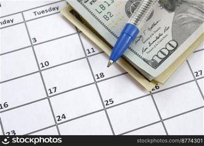 Pen and many hundred US dollar bills on calendar page close up. Business and financial planning concept. Accountant work. Pen and many hundred US dollar bills on calendar page close up