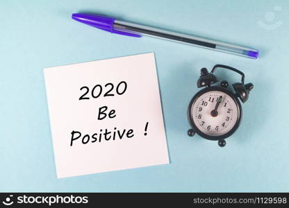 Pen, paper with 2020 be positive and black alarm clock on blue background