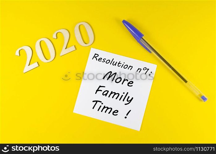Pen, paper with resolution more family time and 2020 in wooden figures on yellow background