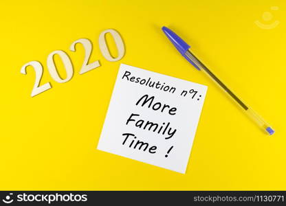 Pen, paper with resolution more family time and 2020 in wooden figures on yellow background
