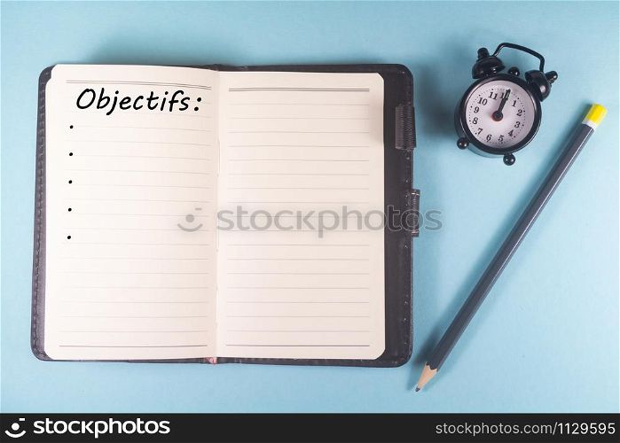 Pencil, notebook with goals written in french language and alarm clock