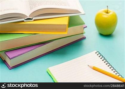 Pencil on notepad with school books and apple on student desk