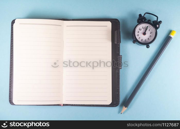 Pencil, open notebook and black alarm clock