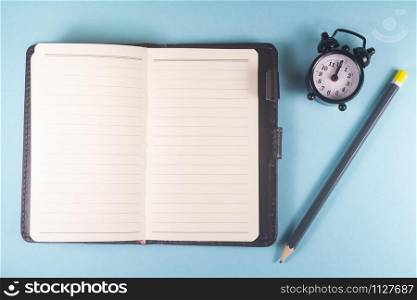 Pencil, open notebook and black alarm clock