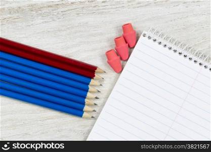 Pencil tips and erasers pointing at a blank spiral notepad on rustic white wood
