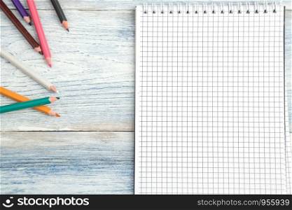 pencils and a paper notebook on a light blue old wooden background. top view. flat lay