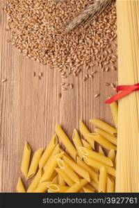 penne and wheat on wooden background