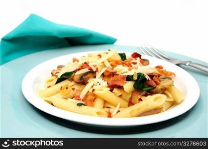 Penne Pasta. Penne pasta with sauteed mushrooms garlic and Spinach with crumbled bacon and grated parmesan cheese severed on a turquoise and white plate combination.