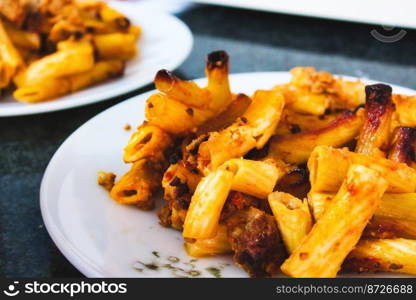 Penne pasta tubes with bolognese sauce on a white plate on a kitchen worktop