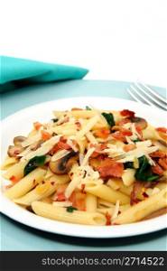 Penne Pasta With Bacon And Mushrooms. Penne pasta with sauteed mushrooms garlic and Spinach with crumbled bacon and grated parmesan cheese severed on a turquoise and white plate combination.