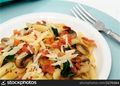 Penne Pasta With Mushrooms. Penne pasta with sauteed mushrooms garlic and Spinach with crumbled bacon and grated parmesan cheese severed on a turquoise and white plate combination.