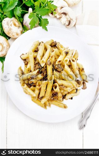 Penne pasta with wild mushrooms in a plate, towel, parsley and fork on a light wooden board background from above