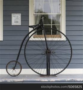 Penny farthing bicycle against house on sidewalk, Sherbrooke, Nova Scotia, Canada