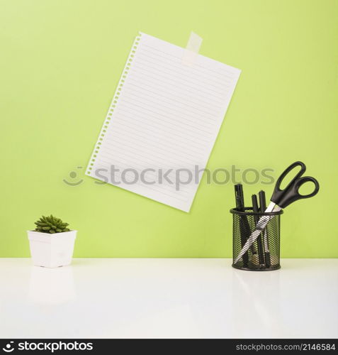 pens scissors holder near paper stucked green wall