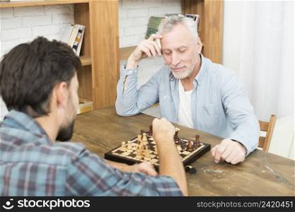 pensive aged man young guy playing chess table near bookshelves