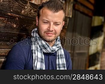 Pensive attractive man leaning against wooden wall fashion relaxing scarf
