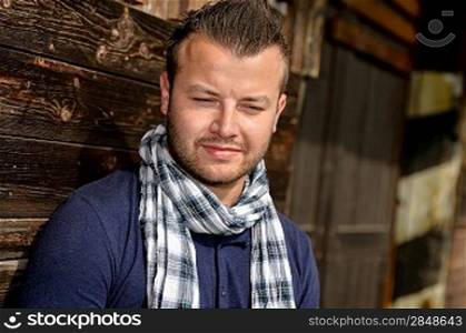 Pensive attractive man leaning against wooden wall fashion relaxing scarf