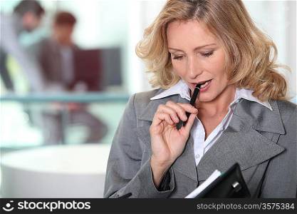 Pensive blond businesswoman chewing on pen