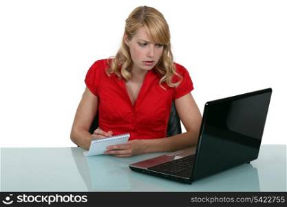 Pensive blond woman taking notes from laptop screen