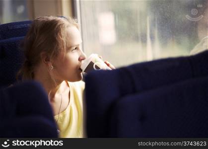 Pensive blond young woman drinking coffee and looking out the window while traveling by train