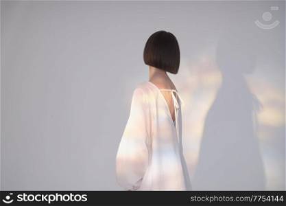 Pensive brunette in a white dress in the light of sunbeams