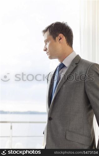 Pensive businessman standing by glass door in hotel