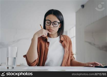 Pensive female housewife calculates expenses, planning household budget for economy saving money. Focused woman tenant calculating housekeeping costs, the rent, electricity, sitting at desk at home.. Female housewife in glasses calculates expenses, planning household budget for saving money at home