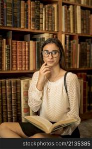 pensive female student sitting with book library