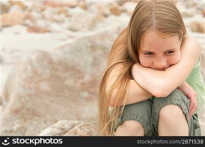 Pensive girl (10-12) sitting on rock on beach