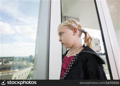 Pensive girl in vampire costume looking out through window at home