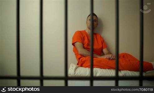 Pensive inmate sits on bed in prison