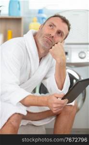 pensive man wearing bathrobe doing laundry