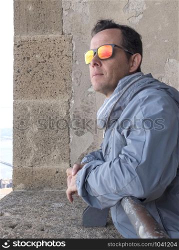 Pensive man wearing sunglasses leaning on a vintage window looking outdoors
