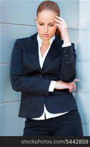 Pensive modern business woman with hand near head standing at office building&#xA;